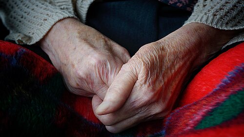 An elderly person's hands clasped together over a blanket