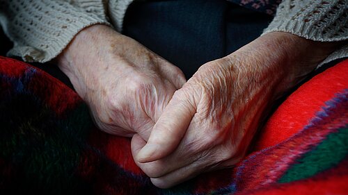 An elderly person's hands clasped together over a blanket
