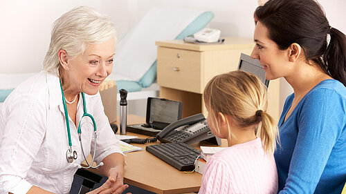 A mother holding a child whilst speaking to a GP